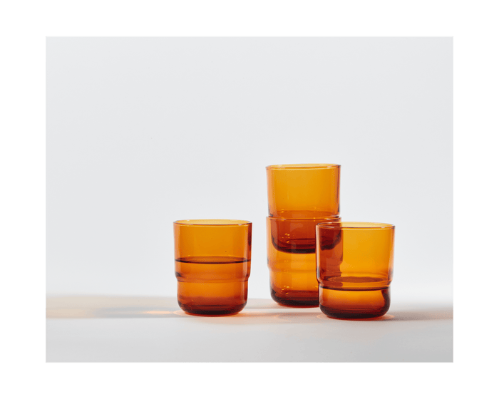 Three Short Night + Day Glasses made of amber recycled glass are arranged on a white surface, with two stacked and one placed beside them.