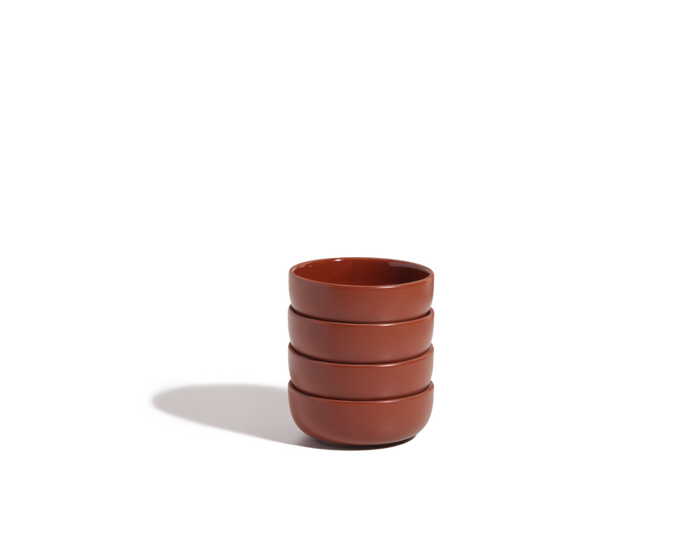 A stack of four Tiny Bowls, crafted from brown ceramic and designed for modern tableware settings, is arranged on a plain white background with a shadow cast to the left.
