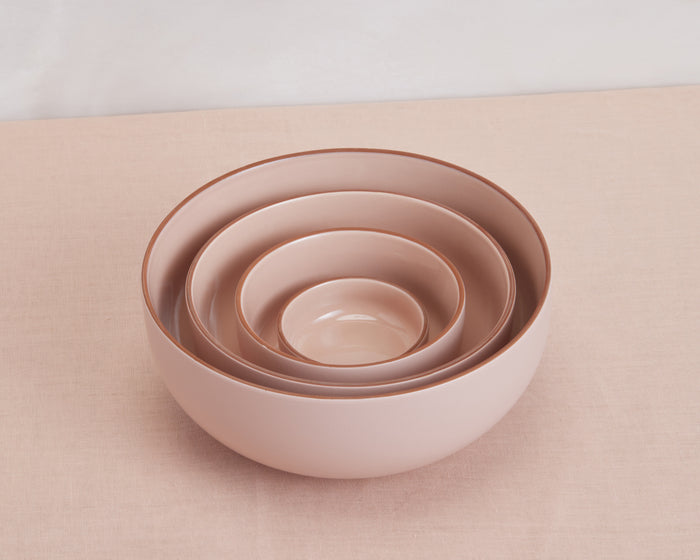 Four pink ceramic Tiny Bowls of varying sizes are stacked together on a light pink fabric, showcasing this elegant and stackable tableware set.
