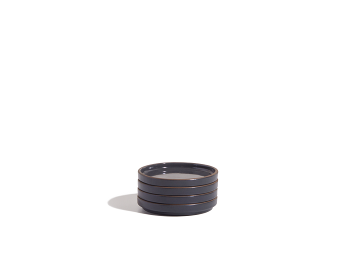 The Tiny Plates are small, round, dark-colored ceramic dishes with three horizontal ridges, ideal for serving snacks or adding to your tableware set. Set against a plain white background.