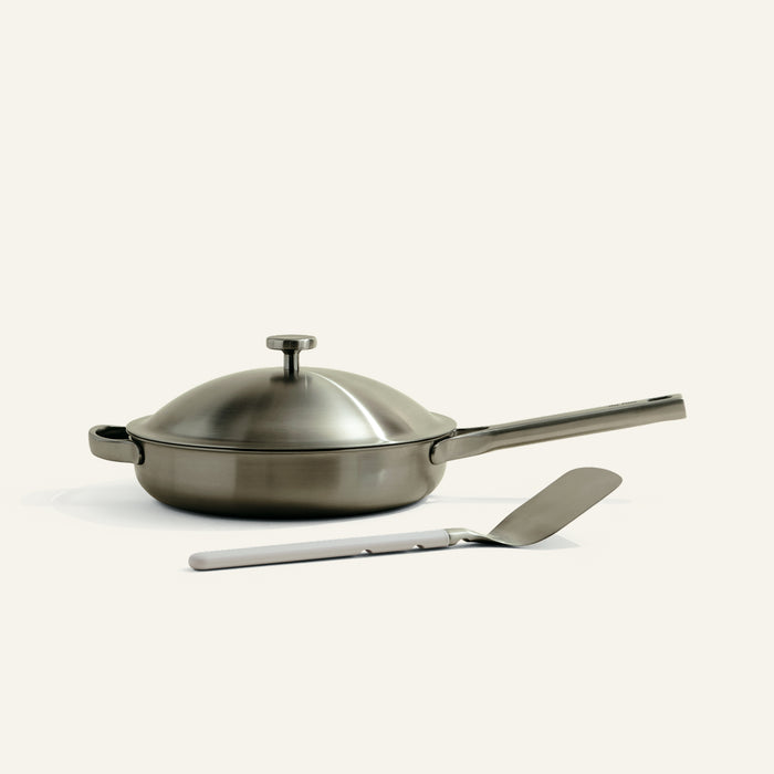 Stainless steel frying pan with lid and spatula on a white background