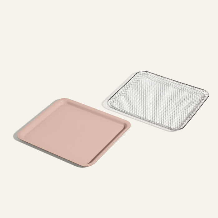 The Wonder Oven Essentials Kit features a pink nonstick ceramic bake pan placed beside a silver rectangular wire rack, resembling an air fryer basket, on a simple light background.