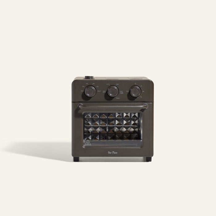 The Wonder Oven is a compact black air fryer toaster oven featuring three control knobs and a diamond-patterned glass door, displayed against a plain light background.