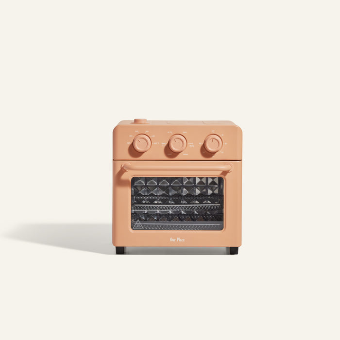 The Wonder Oven is a compact, peach-colored countertop toaster oven featuring three control knobs and a clear front door, shown against a plain off-white background.