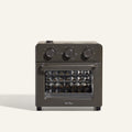 The Wonder Oven is a black countertop toaster oven with steam infusion, three control knobs on top, a glass door, and "Our Place" printed near the bottom.