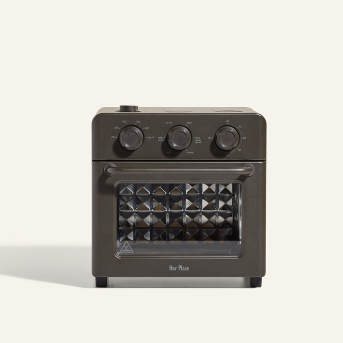 The Wonder Oven is a black countertop toaster oven with steam infusion, three control knobs on top, a glass door, and "Our Place" printed near the bottom.